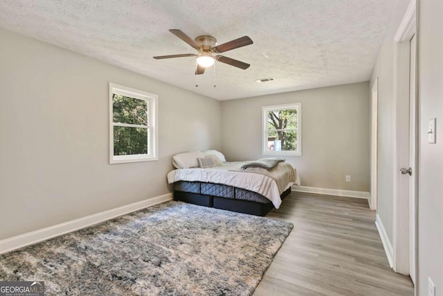 bedroom with light hardwood / wood-style flooring, a textured ceiling, and ceiling fan