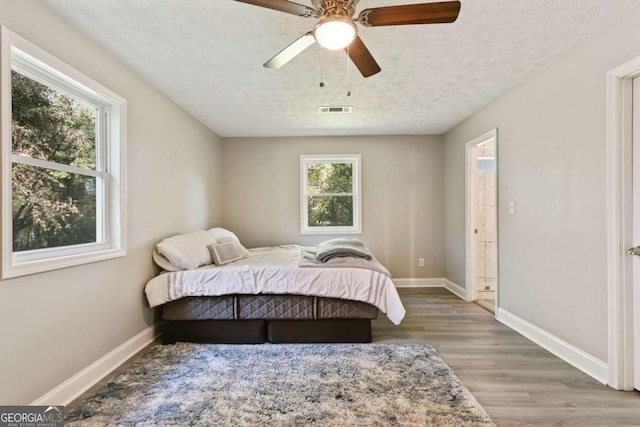 bedroom with a textured ceiling, hardwood / wood-style flooring, multiple windows, and ceiling fan