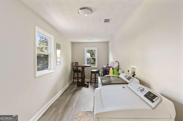 clothes washing area with a textured ceiling, a healthy amount of sunlight, wood-type flooring, and washer and clothes dryer