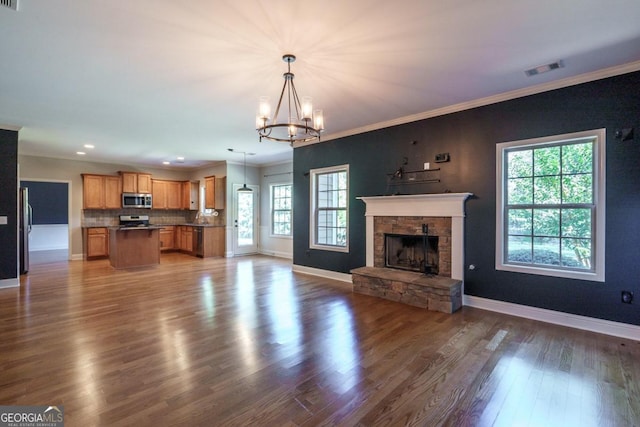 unfurnished living room with a healthy amount of sunlight, a chandelier, dark hardwood / wood-style floors, and a stone fireplace