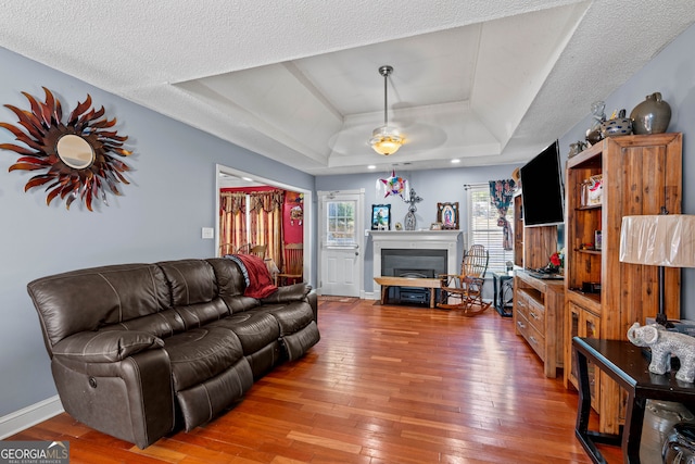 living room with a textured ceiling, wood-type flooring, a tray ceiling, and ceiling fan