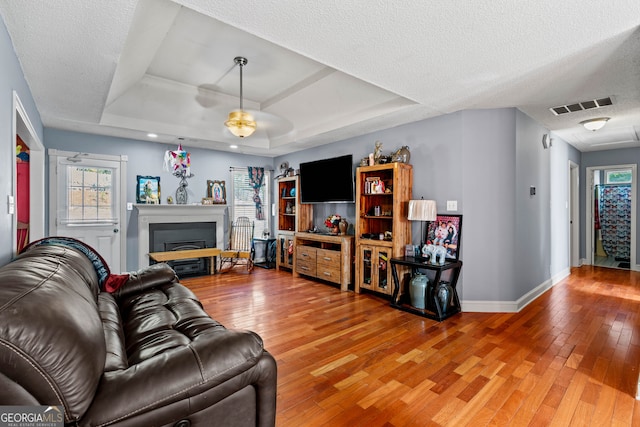 living room with a textured ceiling, hardwood / wood-style flooring, and a raised ceiling