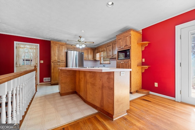 kitchen featuring a textured ceiling, stainless steel fridge, light hardwood / wood-style floors, ornamental molding, and black microwave