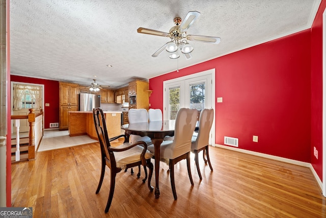 dining room featuring ceiling fan, a textured ceiling, ornamental molding, and light wood-type flooring