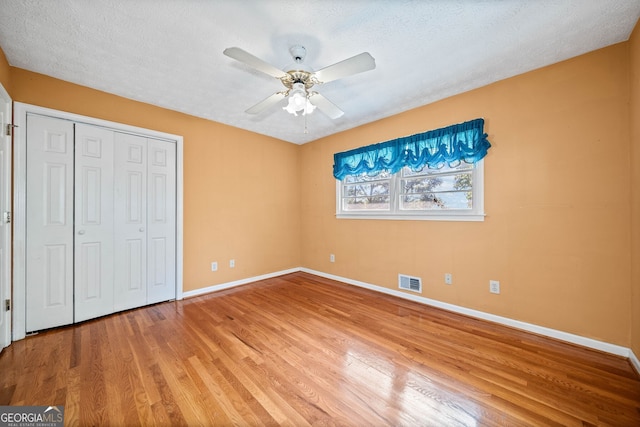 unfurnished bedroom with a closet, ceiling fan, wood-type flooring, and a textured ceiling