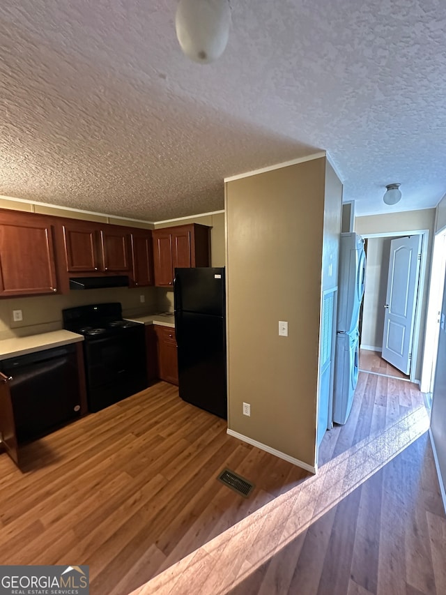 kitchen with a textured ceiling, black appliances, and light hardwood / wood-style flooring