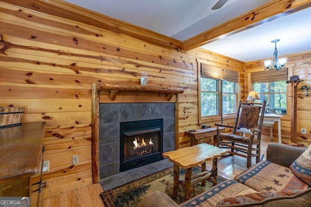 living room with a notable chandelier, wooden walls, wood-type flooring, and a tile fireplace