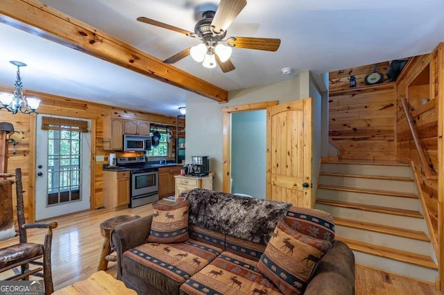 living room featuring light hardwood / wood-style flooring, wood walls, and ceiling fan with notable chandelier