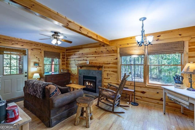 living room with wood walls, beamed ceiling, ceiling fan with notable chandelier, a fireplace, and light hardwood / wood-style floors