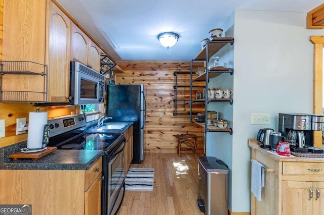 kitchen featuring light hardwood / wood-style floors, stainless steel appliances, sink, and wooden walls