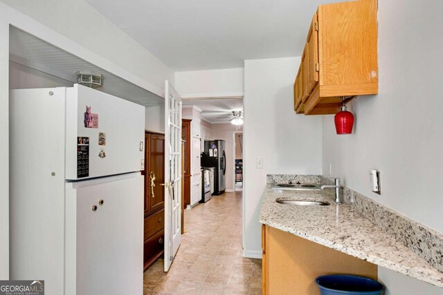 kitchen with sink, white refrigerator, light stone counters, stainless steel refrigerator, and ceiling fan