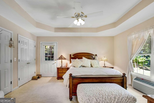 bedroom featuring ceiling fan, a raised ceiling, light carpet, and a wall mounted air conditioner