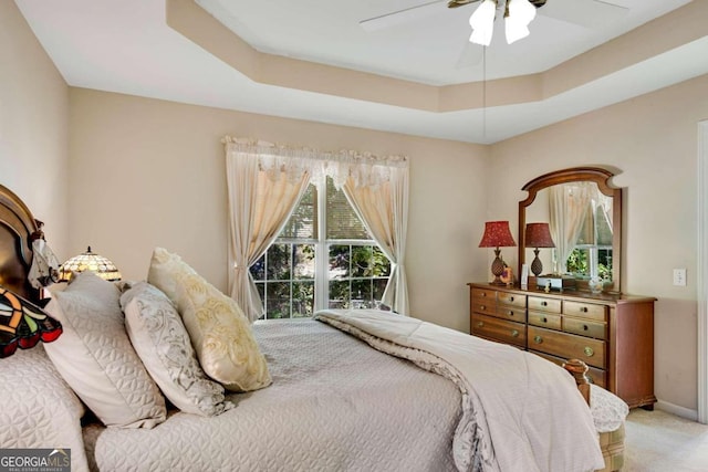 carpeted bedroom with multiple windows, a raised ceiling, and ceiling fan