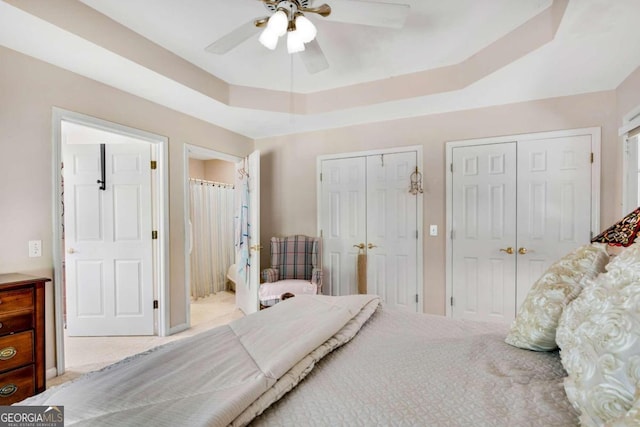 bedroom with a tray ceiling, light colored carpet, connected bathroom, and ceiling fan