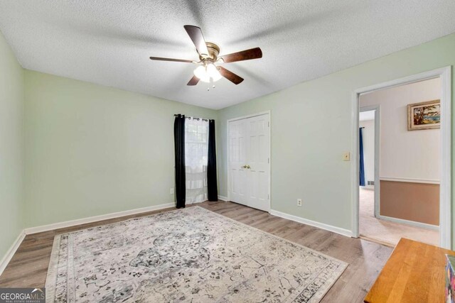 unfurnished bedroom featuring a closet, ceiling fan, wood-type flooring, and a textured ceiling