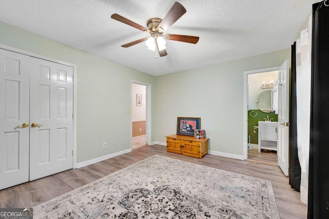 unfurnished bedroom with a closet, a textured ceiling, ensuite bathroom, light hardwood / wood-style floors, and ceiling fan