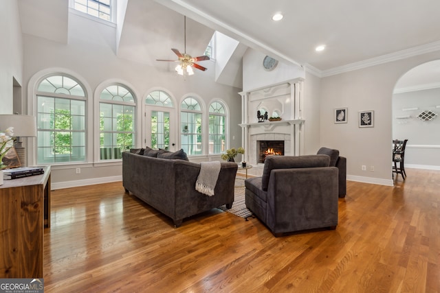 living room with hardwood / wood-style floors, ceiling fan, a fireplace, a towering ceiling, and crown molding