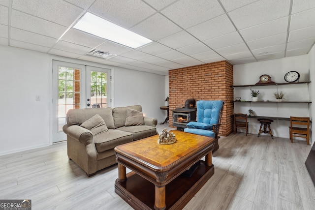 living room featuring light hardwood / wood-style floors, a wood stove, french doors, and a drop ceiling