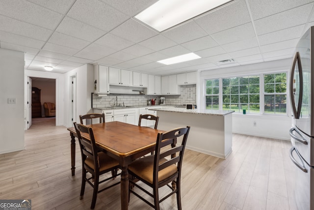 dining area with sink, a paneled ceiling, and light wood-type flooring