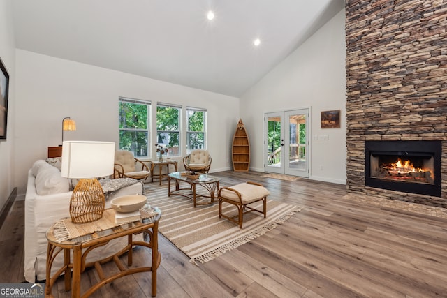 living room with french doors, high vaulted ceiling, a stone fireplace, and light hardwood / wood-style flooring