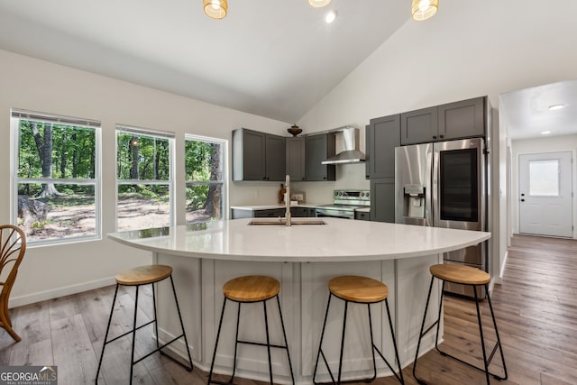 kitchen featuring a kitchen bar, stainless steel appliances, wall chimney exhaust hood, gray cabinets, and light hardwood / wood-style flooring