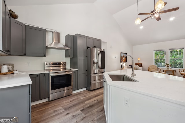 kitchen featuring appliances with stainless steel finishes, sink, light hardwood / wood-style floors, wall chimney exhaust hood, and decorative light fixtures