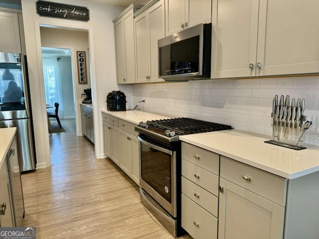 kitchen with light hardwood / wood-style floors, tasteful backsplash, stainless steel appliances, and gray cabinets