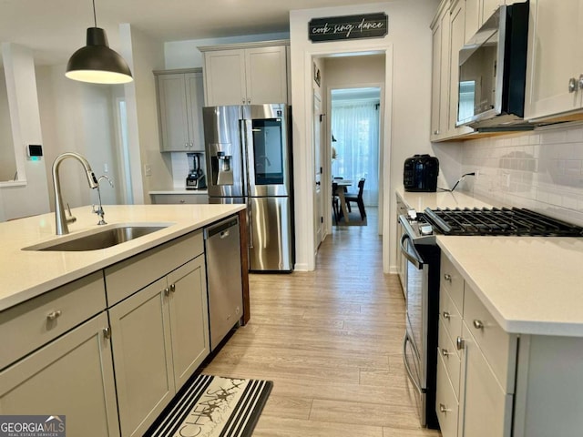 kitchen with gray cabinetry, appliances with stainless steel finishes, sink, and light wood-type flooring