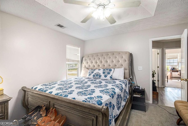 carpeted bedroom featuring a textured ceiling, ceiling fan, and a tray ceiling