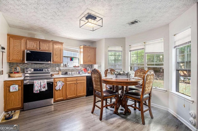 kitchen with sink, a textured ceiling, hardwood / wood-style flooring, decorative backsplash, and appliances with stainless steel finishes