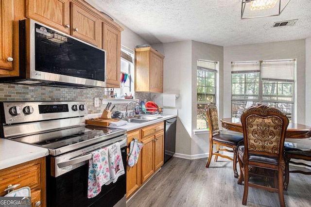 kitchen with wood-type flooring, stainless steel appliances, a textured ceiling, sink, and tasteful backsplash