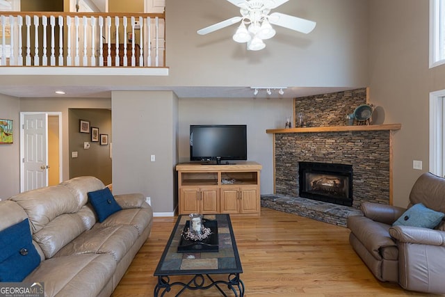 living room featuring ceiling fan, a high ceiling, light hardwood / wood-style flooring, and a stone fireplace