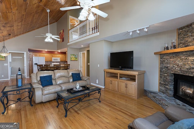 living room featuring ceiling fan, light hardwood / wood-style flooring, wood ceiling, a stone fireplace, and high vaulted ceiling