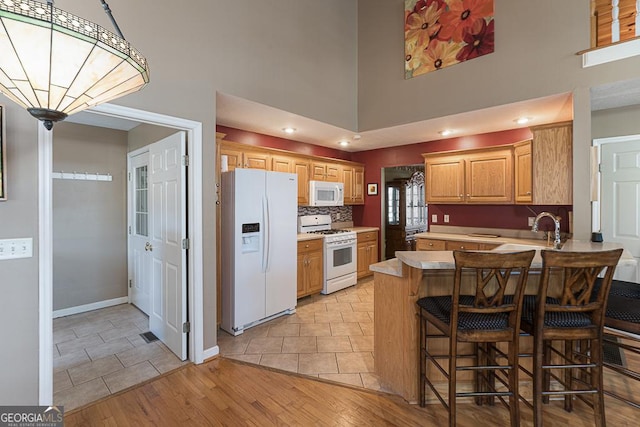 kitchen featuring white appliances, tasteful backsplash, kitchen peninsula, a breakfast bar, and light hardwood / wood-style flooring