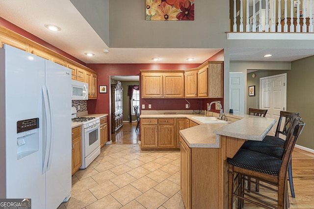 kitchen with a breakfast bar, kitchen peninsula, decorative backsplash, sink, and white appliances