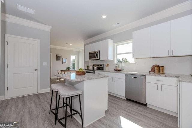 kitchen with a kitchen island, light hardwood / wood-style flooring, light stone countertops, white cabinetry, and appliances with stainless steel finishes