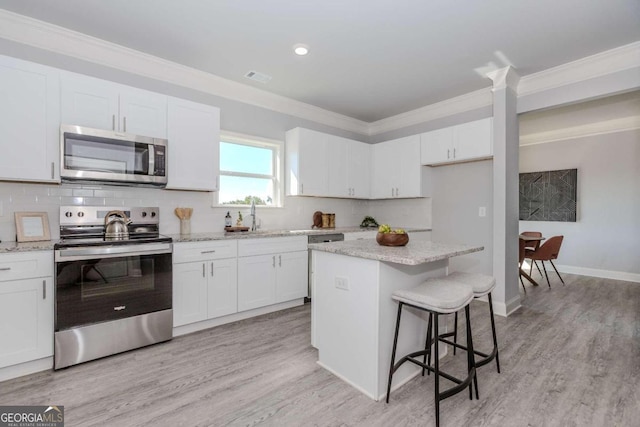 kitchen with white cabinets, stainless steel appliances, light hardwood / wood-style floors, crown molding, and a center island