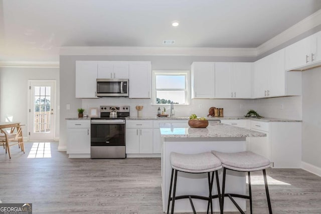 kitchen with ornamental molding, white cabinetry, stainless steel appliances, and light wood-type flooring