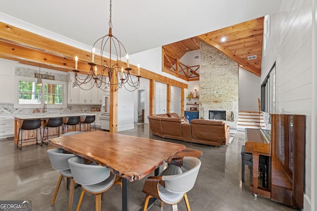 dining area with an inviting chandelier, sink, high vaulted ceiling, and a large fireplace