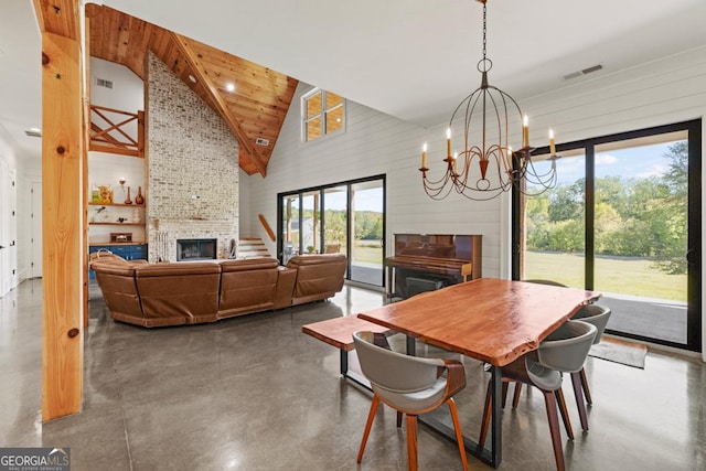 dining area with an inviting chandelier, wooden walls, high vaulted ceiling, concrete flooring, and a fireplace