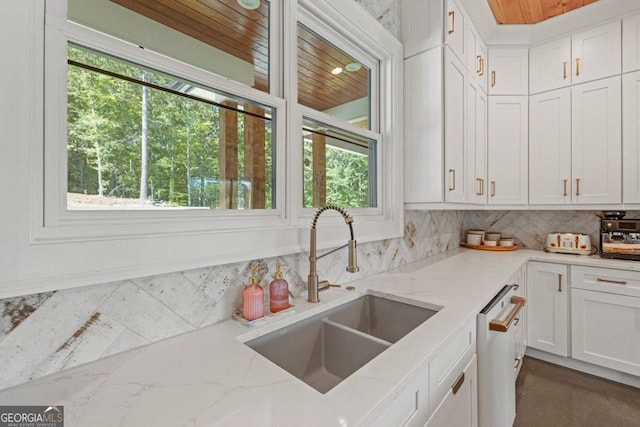 kitchen featuring sink, light stone counters, white dishwasher, decorative backsplash, and white cabinets