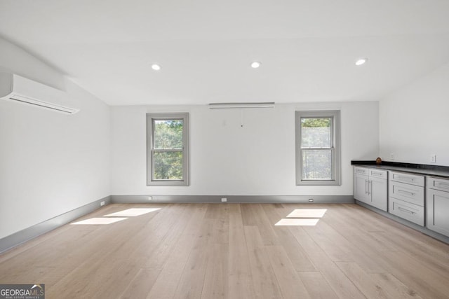 spare room featuring a wall mounted air conditioner, light hardwood / wood-style floors, and plenty of natural light