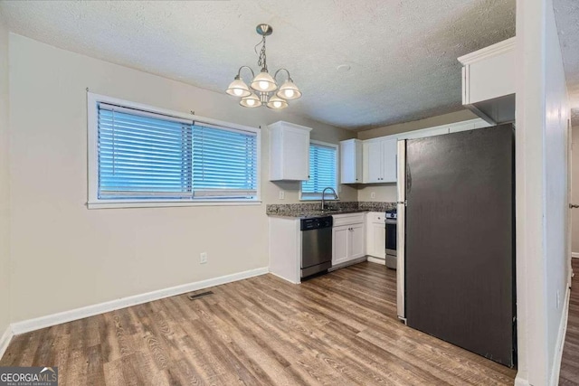 kitchen with appliances with stainless steel finishes, white cabinetry, pendant lighting, light hardwood / wood-style floors, and sink