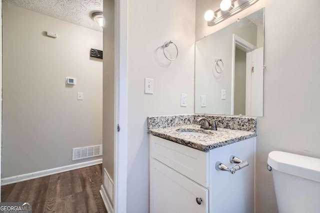 bathroom with toilet, a textured ceiling, hardwood / wood-style flooring, and vanity