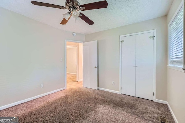 unfurnished bedroom featuring a closet, ceiling fan, a textured ceiling, and light colored carpet