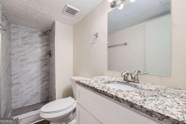 bathroom featuring vanity, tiled shower, a textured ceiling, and toilet