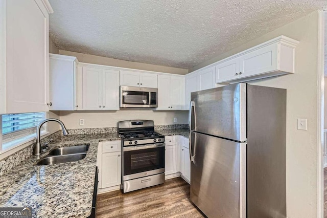 kitchen with sink, hardwood / wood-style floors, stainless steel appliances, white cabinets, and light stone counters