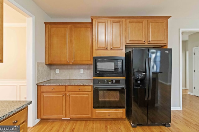 kitchen with tasteful backsplash, black appliances, light stone countertops, and light wood-type flooring