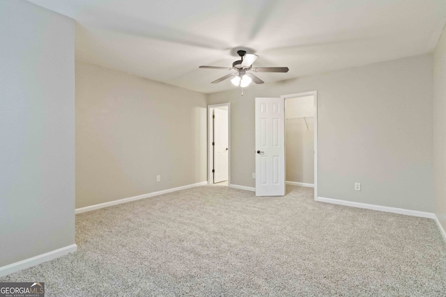 unfurnished bedroom with carpet, a walk in closet, a closet, and ceiling fan