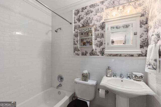 bathroom featuring toilet, tiled shower / bath combo, ornamental molding, and tile walls